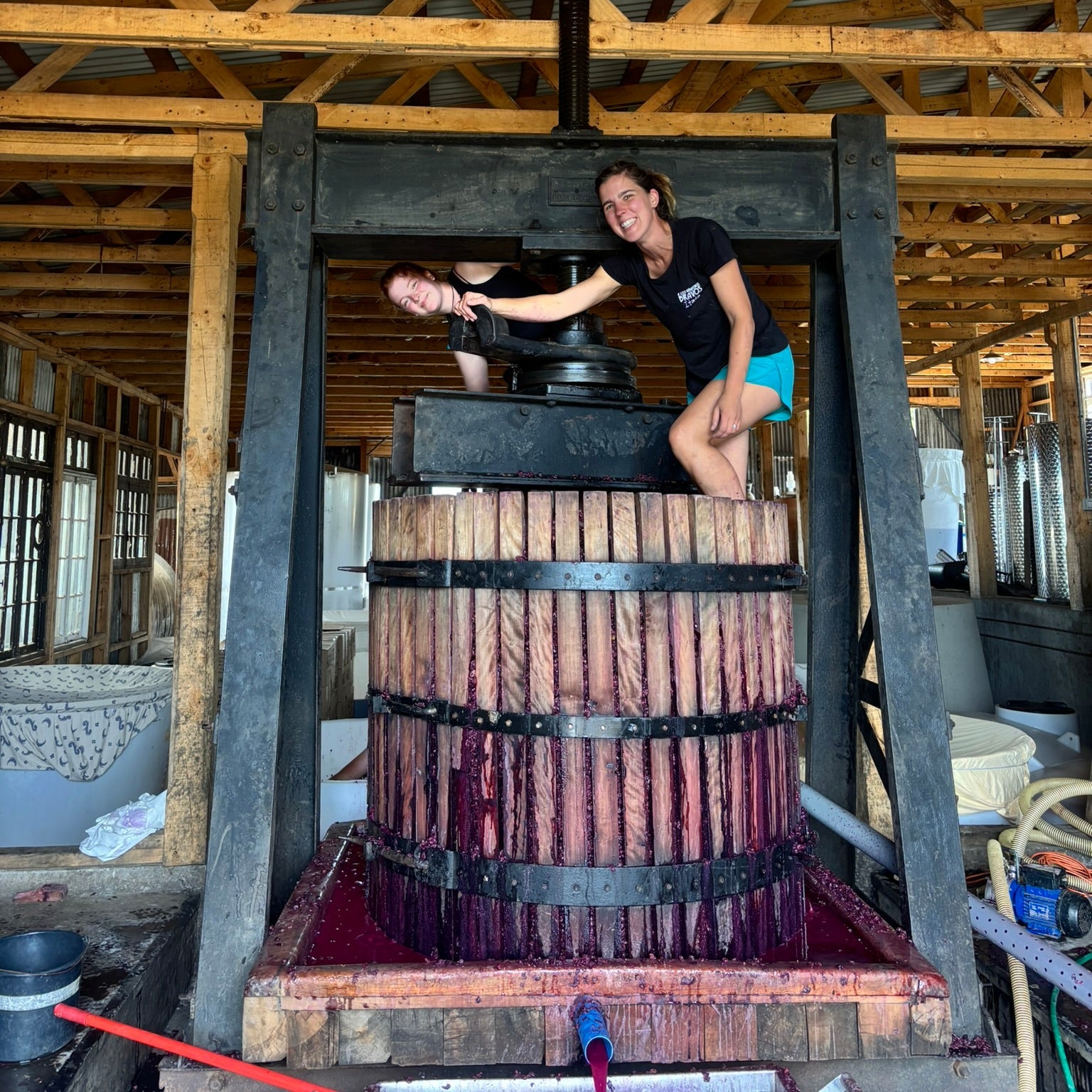 Zjos operating a large wooden press inside a rustic building.